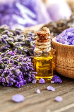 Ahşap bir masanın üzerinde kurutulmuş lavanta çiçekleri olan lavanta spa ürünleri. Tahta zemine banyo tuzu ve masaj yağı serpiştirilmiş. Cilt bakımı, güzellik tedavi konsepti. Lavendula oleum