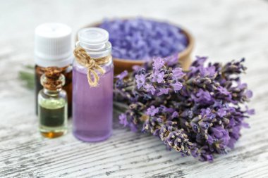 Ahşap bir masanın üzerinde kurutulmuş lavanta çiçekleri olan lavanta spa ürünleri. Tahta zemine banyo tuzu ve masaj yağı serpiştirilmiş. Cilt bakımı, güzellik tedavi konsepti. Lavendula oleum