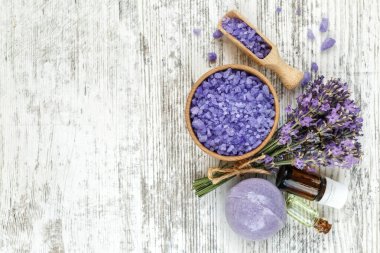 Ahşap bir masanın üzerinde kurutulmuş lavanta çiçekleri olan lavanta spa ürünleri. Tahta zemine banyo tuzu ve masaj yağı serpiştirilmiş. Cilt bakımı, güzellik tedavi konsepti. Lavendula oleum