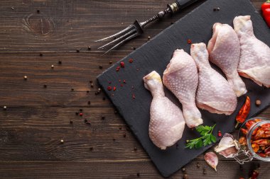 Katalog için çekim yapıyorum. Tahta bir tahtanın üzerinde baharatlı ve sebzeli çiğ tavuk bacağı. Siyah arka plan. Üst görünüm