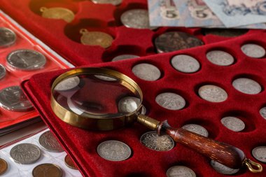 Numismatics. Old collectible coins made of silver on a wooden table.Coins in the album.Collection of old coins. Magnifying glass clipart