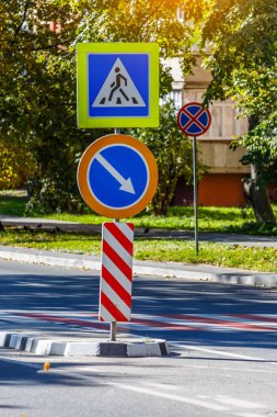Yol işaretleri! Güneşli bir bahar gününde, şehrin arka planında ve parkında yaya geçidi. Yoldan geçen çocuklar için trafik işareti uyarısı.