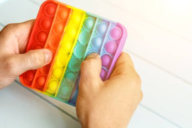 Bir erkeğin eli renkli bir gökkuşağına basar. Silikon anti-stres oyuncağı. Rahatlama, çok renkli duyusal oyuncak. Çocuklar ve yetişkinler için yeni bir duyusal stres önleyici oyuncak..