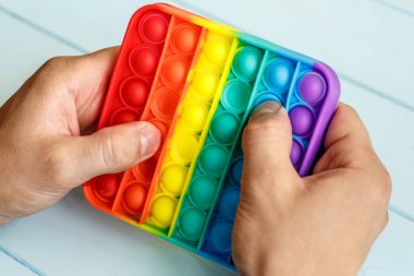 Bir erkeğin eli renkli bir gökkuşağına basar. Silikon anti-stres oyuncağı. Rahatlama, çok renkli duyusal oyuncak. Çocuklar ve yetişkinler için yeni bir duyusal stres önleyici oyuncak..