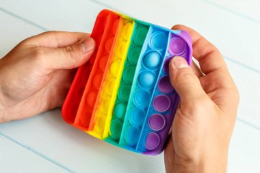 Bir erkeğin eli renkli bir gökkuşağına basar. Silikon anti-stres oyuncağı. Rahatlama, çok renkli duyusal oyuncak. Çocuklar ve yetişkinler için yeni bir duyusal stres önleyici oyuncak..