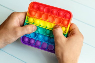 Bir erkeğin eli renkli bir gökkuşağına basar. Silikon anti-stres oyuncağı. Rahatlama, çok renkli duyusal oyuncak. Çocuklar ve yetişkinler için yeni bir duyusal stres önleyici oyuncak..