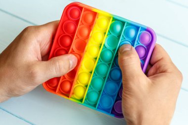 Bir erkeğin eli renkli bir gökkuşağına basar. Silikon anti-stres oyuncağı. Rahatlama, çok renkli duyusal oyuncak. Çocuklar ve yetişkinler için yeni bir duyusal stres önleyici oyuncak..
