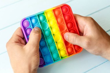Bir erkeğin eli renkli bir gökkuşağına basar. Silikon anti-stres oyuncağı. Rahatlama, çok renkli duyusal oyuncak. Çocuklar ve yetişkinler için yeni bir duyusal stres önleyici oyuncak..