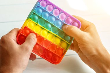 Bir erkeğin eli renkli bir gökkuşağına basar. Silikon anti-stres oyuncağı. Rahatlama, çok renkli duyusal oyuncak. Çocuklar ve yetişkinler için yeni bir duyusal stres önleyici oyuncak..