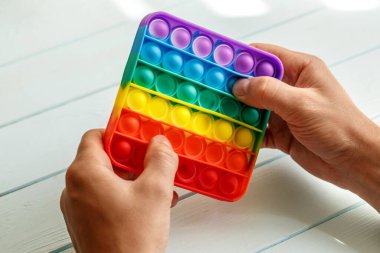 Bir erkeğin eli renkli bir gökkuşağına basar. Silikon anti-stres oyuncağı. Rahatlama, çok renkli duyusal oyuncak. Çocuklar ve yetişkinler için yeni bir duyusal stres önleyici oyuncak..