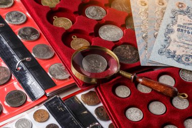 Numismatikler. Tahta bir masanın üzerinde gümüşten yapılmış eski koleksiyon paraları. Albümdeki bozuk paralar. Eski madeni paraların koleksiyonu. Büyüteç