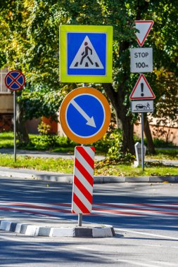 Yol işaretleri! Güneşli bir bahar gününde, şehrin arka planında ve parkında yaya geçidi. Yoldan geçen çocuklar için trafik işareti uyarısı.