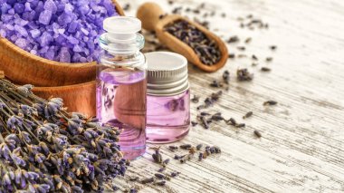 Ahşap bir masanın üzerinde kurutulmuş lavanta çiçekleri olan lavanta spa ürünleri. Tahta zemine banyo tuzu ve masaj yağı serpiştirilmiş. Cilt bakımı, güzellik tedavi konsepti. Lavendula oleum