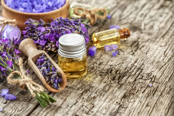 Ahşap bir masanın üzerinde kurutulmuş lavanta çiçekleri olan lavanta spa ürünleri. Tahta zemine banyo tuzu ve masaj yağı serpiştirilmiş. Cilt bakımı, güzellik tedavi konsepti. Lavendula oleum