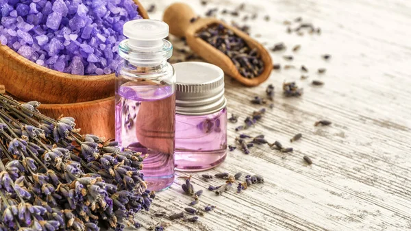 Ahşap bir masanın üzerinde kurutulmuş lavanta çiçekleri olan lavanta spa ürünleri. Tahta zemine banyo tuzu ve masaj yağı serpiştirilmiş. Cilt bakımı, güzellik tedavi konsepti. Lavendula oleum