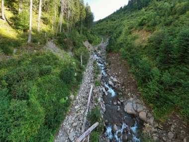 High water flood destroyed a mountain road in the Carpathians, Chornohora, Ukraine. Now a river flows here among boulders and fallen trees. View from the drone to the washed-out road. clipart