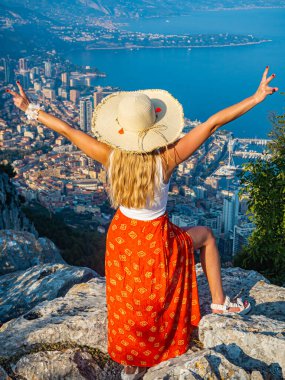 Batan güneş, Monte Carlo, Cote d 'azur, Monaco' nun güzel panoramik manzaralı bir dağda oturan şapkalı genç sarışın kız.