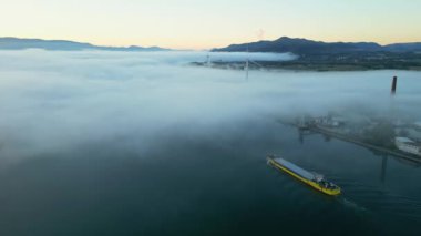 Sabahleyin Rhone Nehri 'nde yoğun siste yüzen bir mavnanın panoramik drone görüntüsü. Fransa 'nın Le Pouzin kasabasında. Arka planda rüzgar santrali