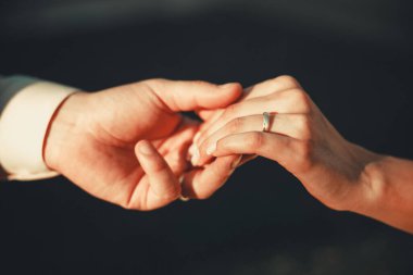 Düğün için. Karanlık arka plandaki erkek ve kadının elleri ılık, yumuşak güneş ışığında. Yeni bir aile doğdu..