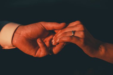 Düğün için. Karanlık arka plandaki erkek ve kadının elleri ılık, yumuşak güneş ışığında. Yeni bir aile doğdu..