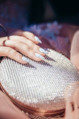 Uzun tırnaklı bir kız parlak beyaz bir çanta tutuyor. Balo günü. Kızın ilk balosu var..