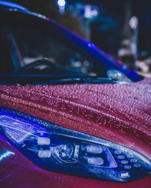 Kırmızı arabaya yağmur damlaları düşer. Neon sokak lambaları arabaların yüzeyine yansıyor. Göz kamaştırıcı gece fotoğrafçılığı.