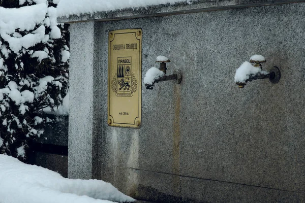 Traduction : Municipalité Pravets. Fontaine d'eau en pierre dans la neige d'hiver. Économisez de l'eau. Jour de la Terre. Source d'eau en Bulgarie. — Photo