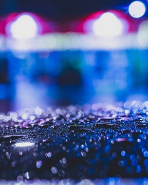 Yansıtıcı yüzeydeki yağmur damlalarının makro görüntüsünü kapat. Arka planda neon ışıkları var. Çarpıcı bir sokak fotoğrafı..