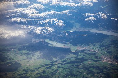 Hareket eden bir uçaktan alınan beyaz bulutlar. Yeşil doğa ve karlı dağlar. Havada uçuyor. Uçak yolculuğu..