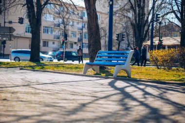 Gündüz güneşinde mavi bank. Bulgaristan 'da sıcak günler. Avrupa 'nın bir şehrinde boş bir ahşap bank. Ağaçlar ve binalar arkasında.