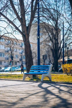Gündüz güneşinde mavi bank. Bulgaristan 'da sıcak günler. Avrupa 'nın bir şehrinde boş bir ahşap bank. Ağaçlar ve binalar arkasında.