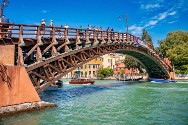 Erkekler ve kadınlar, kanalın üstündeki kemer köprüsünde yelkenli teknelerle geziyorlar.