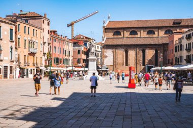 Campo Santo Stefano şehir meydanında eski ampuller ve Campo Santo Stefano heykeliyle yürüyen turistler.