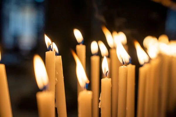 Fileiras de chamas de velas acesas no escuro na igreja para adoração — Fotografia de Stock