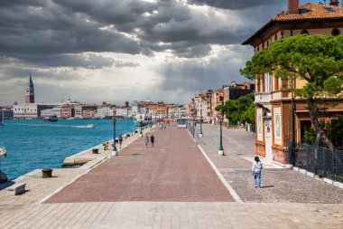 Şehir caddesinde yürüyen gezginler konut binaları ve deniz manzaraları arasında