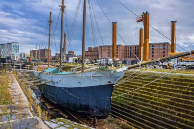 Yelkenli gemi Liverpool 'da demirlemiş, arka planda binalar var.