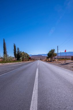 Düz asfalt yolda, arka planda dağlar var.