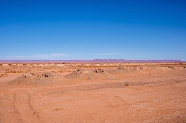Çöldeki kum tepelerinin manzarası ve arka planda dağlar.