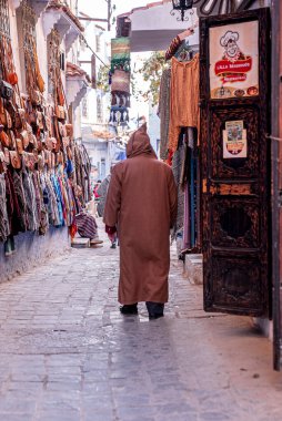 Dar sokakta satılık giysiler ve el çantası duvarda asılı.