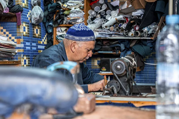 Tailor man in blue prayer cap stitching clothes with sewing machine at shop — Stock Photo, Image