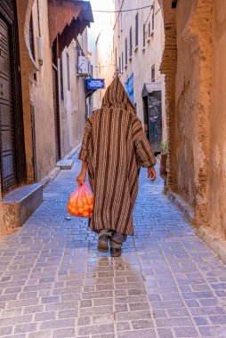 Rear view of man walking in traditional hood clothing while carrying oranges