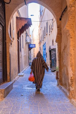 Rear view of man walking in traditional hood clothing while carrying oranges