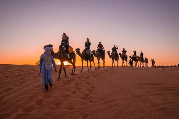 Bedouin leads caravan of camels with tourists through the sand in desert — Stock Photo, Image