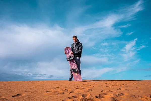 Man with sandboard standing on sand dunes in desert against cloudy sky — Foto Stock