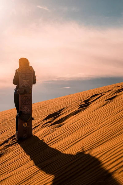 Woman with sandboard standing on sand dunes in desert against cloudy sky — Fotografia de Stock