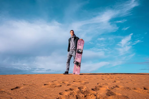 Man with sandboard standing on sand dunes in desert against cloudy sky — Stok fotoğraf