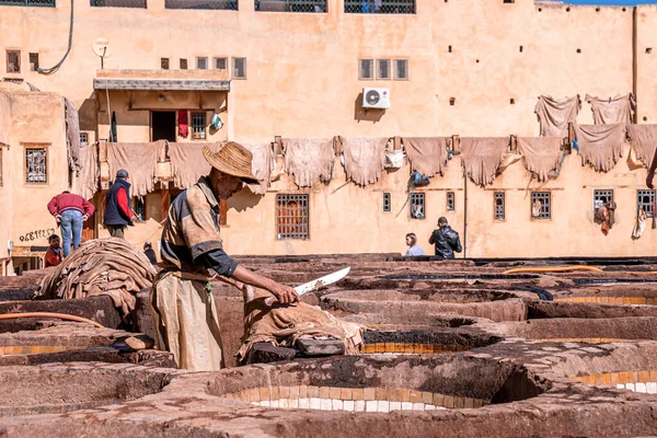 Man working in tannery using knife amidst brims of old stone water baths