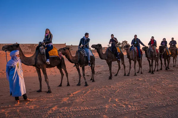 Bedouin in traditional dress leading tourists mounted on camels to ride off — Stok fotoğraf