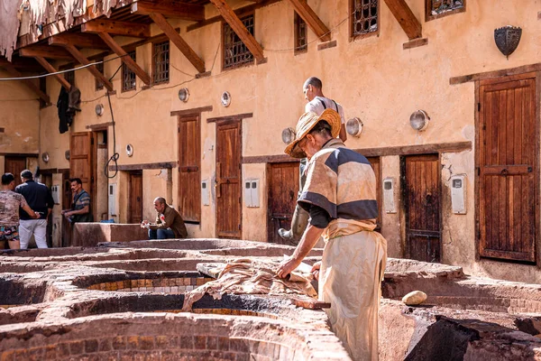 Man working in tannery using knife amidst brims of old stone water baths