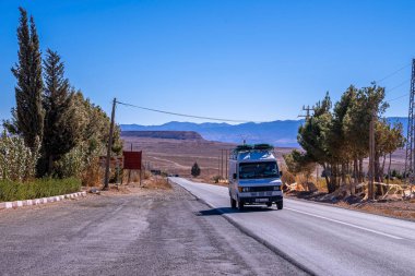 Van travelling on rural road by deserted land against blue sky